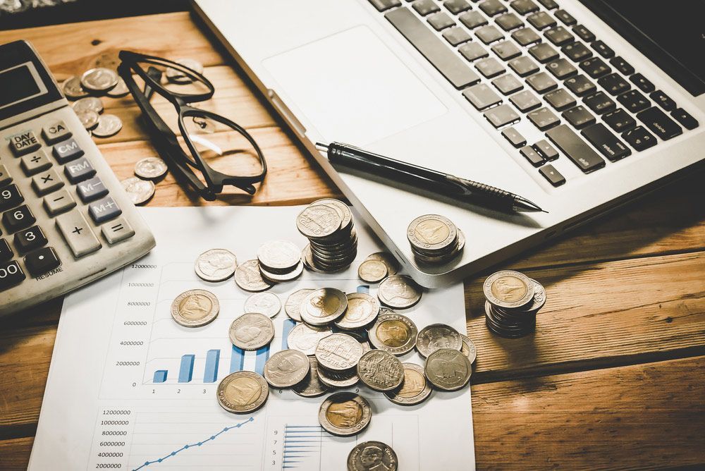 Laptop, Calculator, Coins, Glasses and Pen on A Wooden Desk — Freedom Wealth Solutions In Mornington, VIC