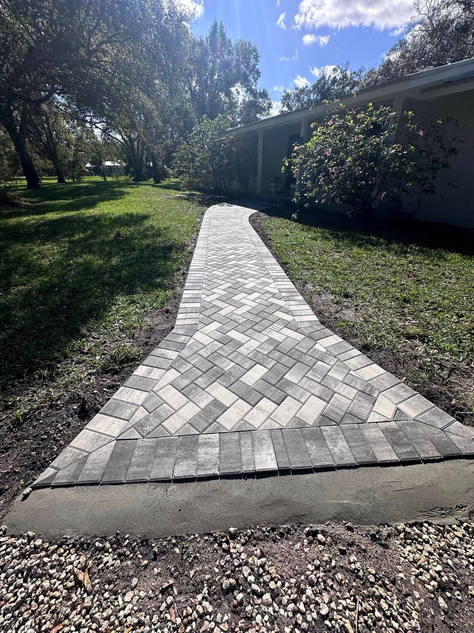 Brick pathway leading to a house, flanked by grass and trees.