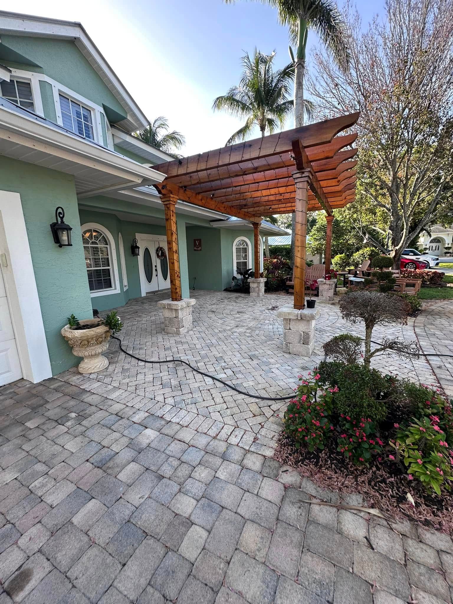 A home with a brown wooden pergola, stone patio, and green exterior paint.