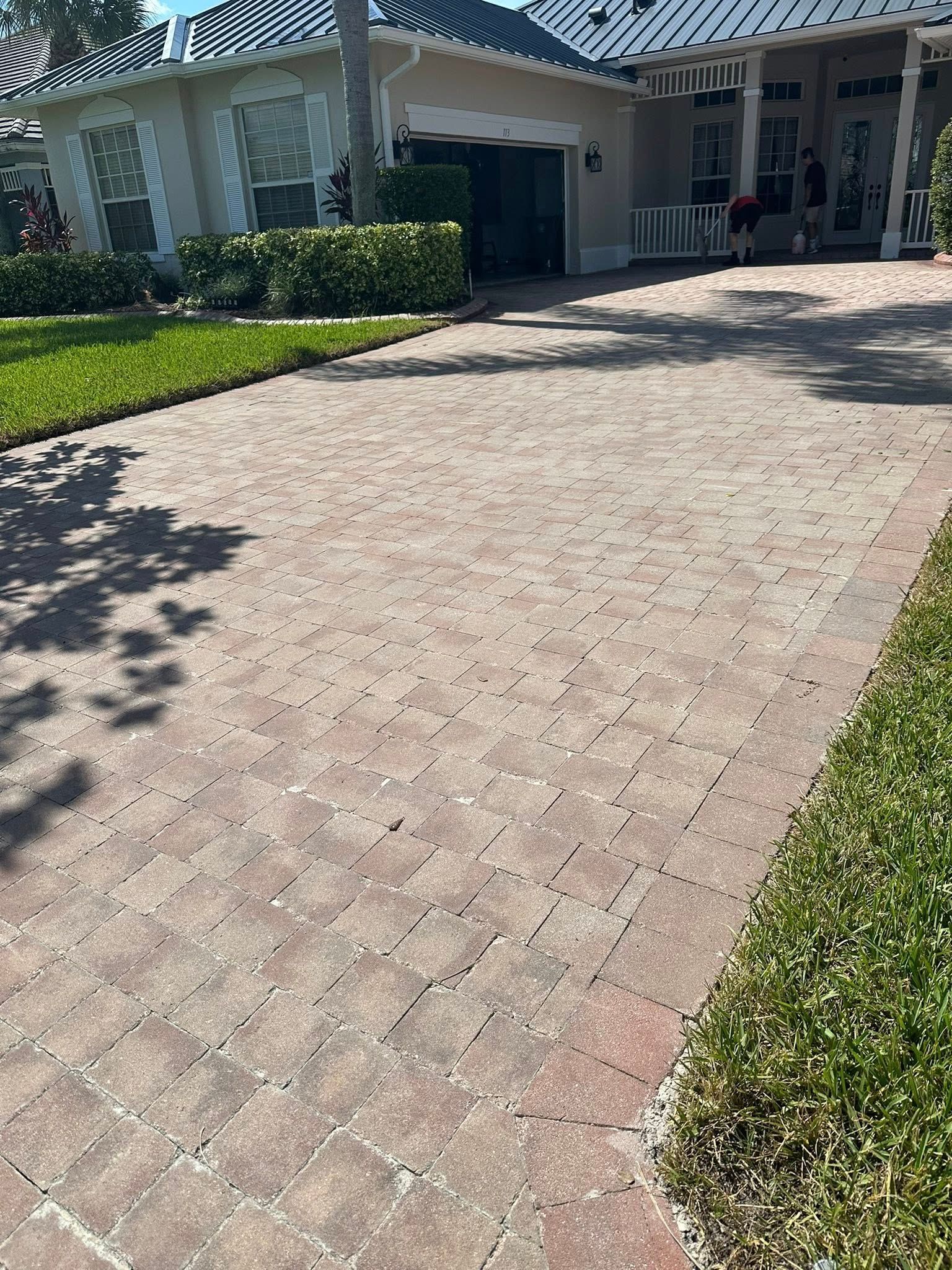 Brick paver driveway leading to a house with a garage and green lawn.