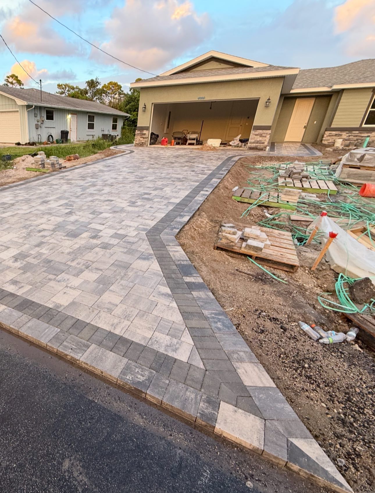 Driveway under construction with gray and light-colored pavers, leading to a house with a garage.