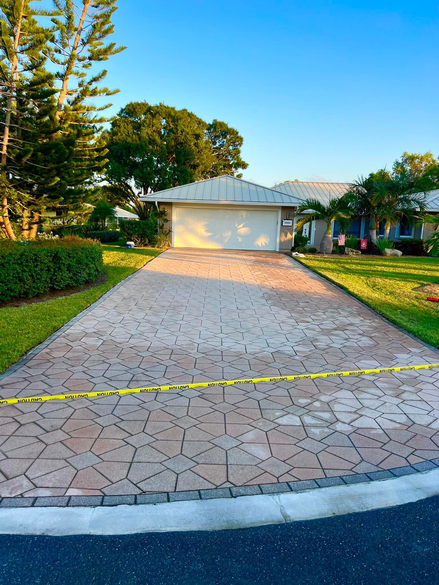 Driveway paved with textured bricks leads to a one-story house with a white garage door. Yellow caution tape.