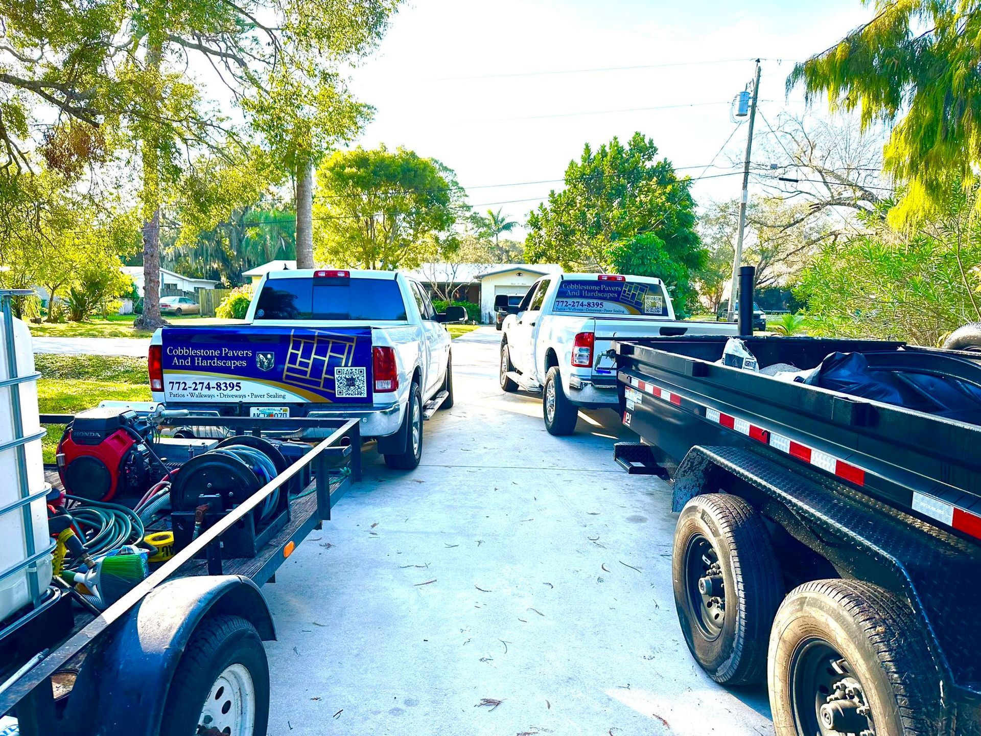 Two trucks and trailers parked on a driveway; one truck has a company logo on the back.