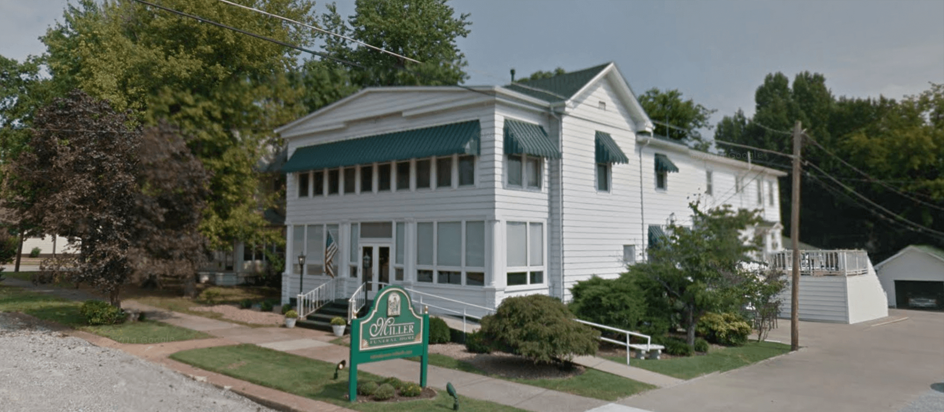 White building with green awnings, sign, and landscaping.