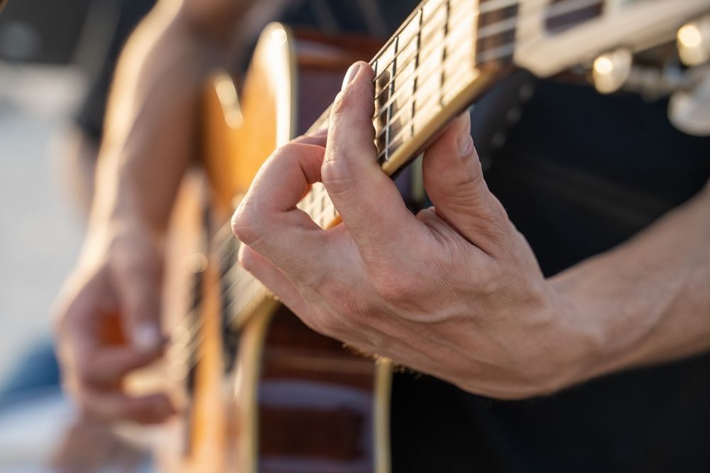 Person's hands playing an acoustic guitar, fingers pressing down on the frets.
