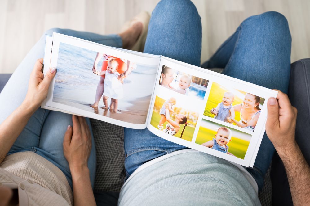 Couple sitting on a couch, looking at a photo album filled with family pictures.
