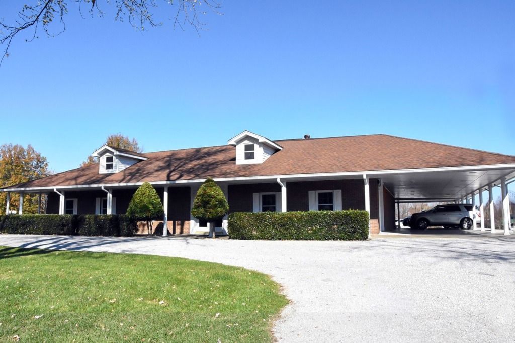 A one-story brown house with a carport and a car parked in it, green lawn in front.