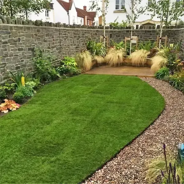 A garden with a stone wall and a lush green lawn.