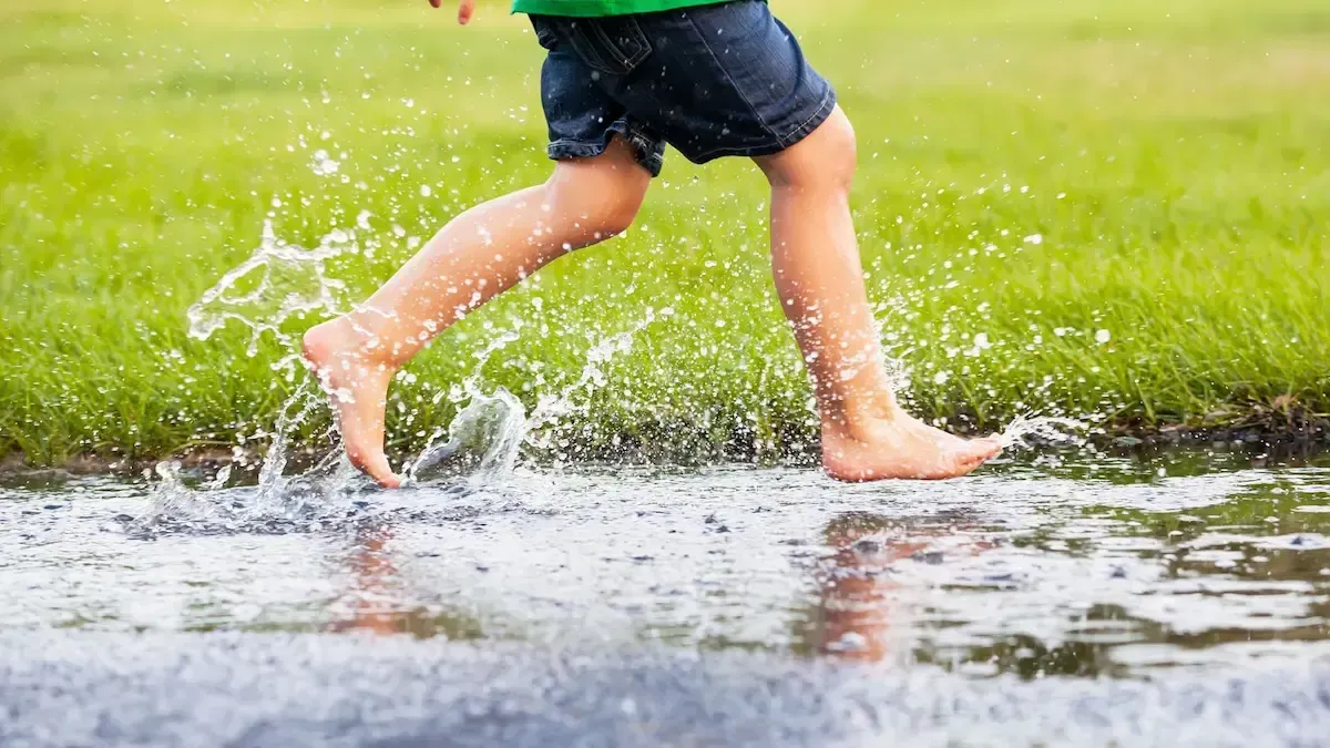 A young boy is running through a puddle of water.