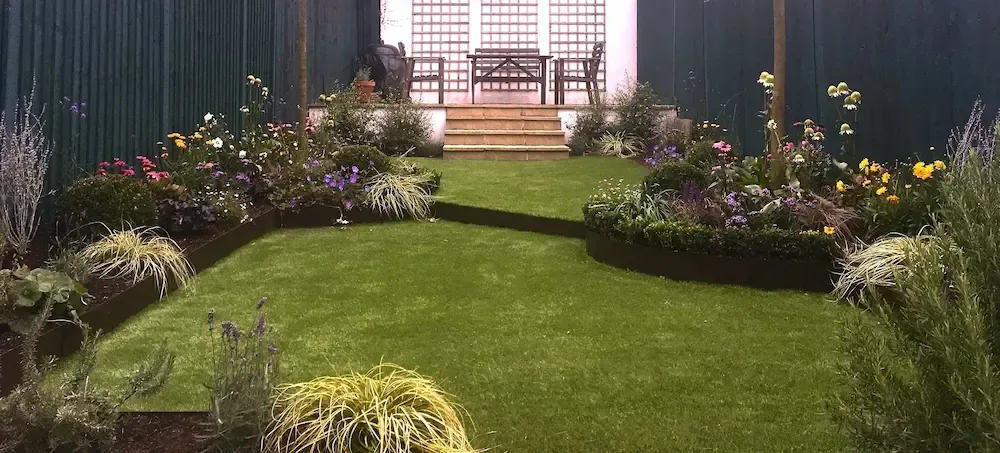 A lush green lawn with flowers and a bench in the background.