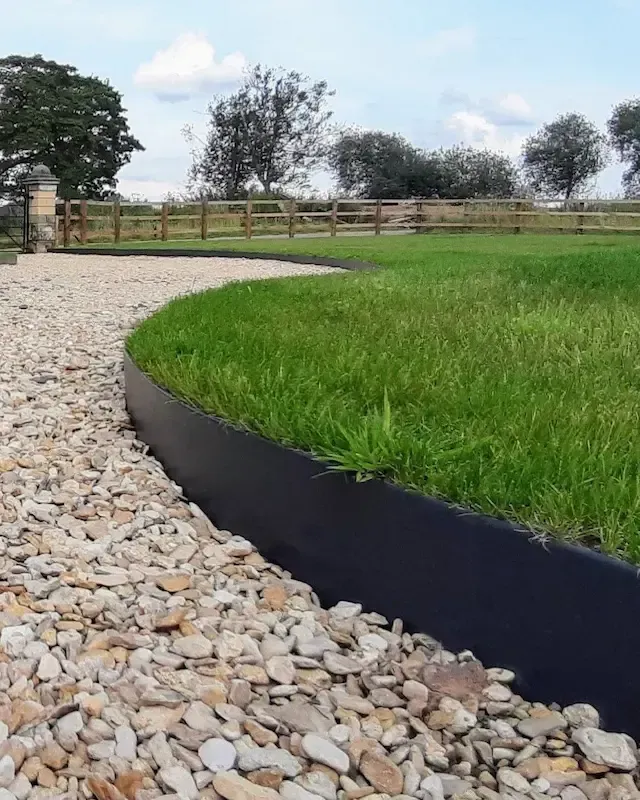 a lawn with a black edging surrounded by gravel and grass .