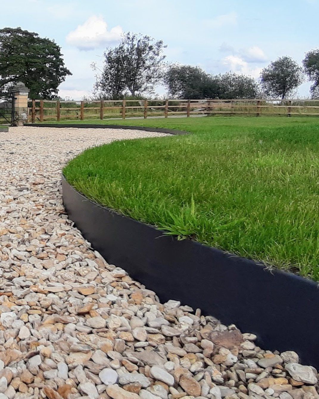 a lawn with a black edging surrounded by gravel and grass .