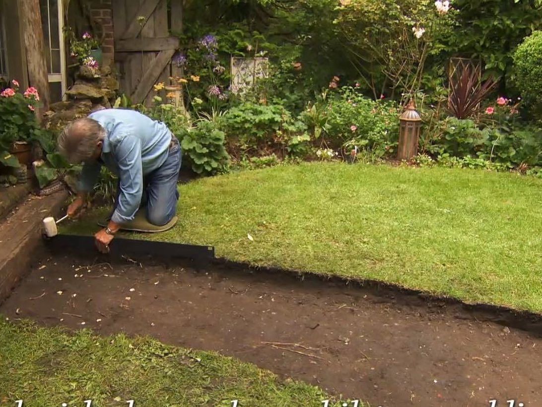 Man installing edging along a lawn path in a garden.