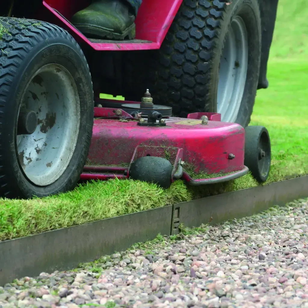 A red lawn mower is cutting grass on a gravel road