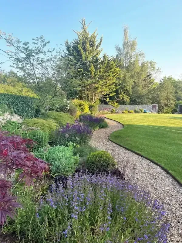 A gravel path in a garden surrounded by flowers and trees.