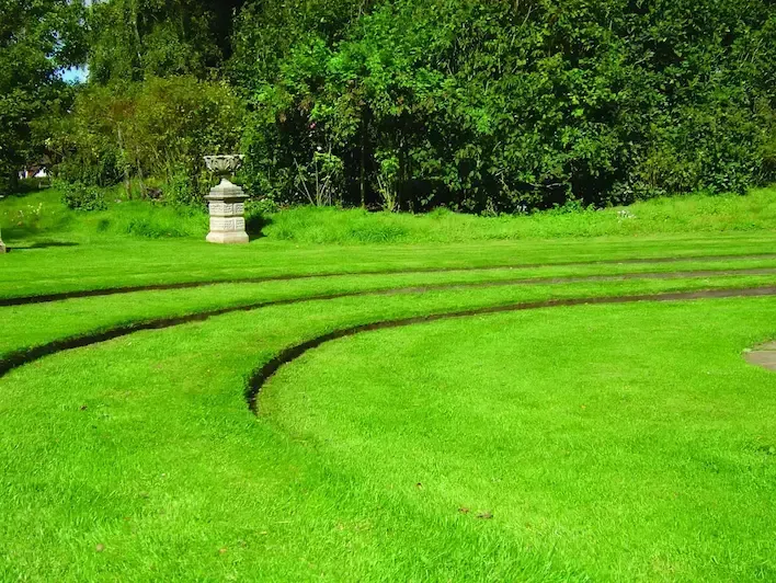 A lush green field with a statue in the middle and trees in the background.