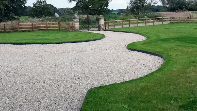 A gravel driveway going through a lush green field.