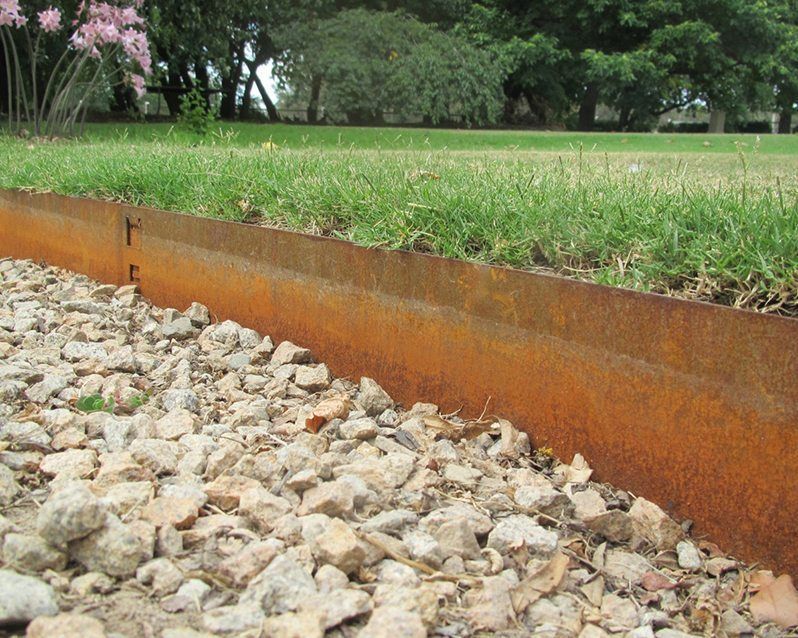 a rusty metal fence is surrounded by gravel and grass
