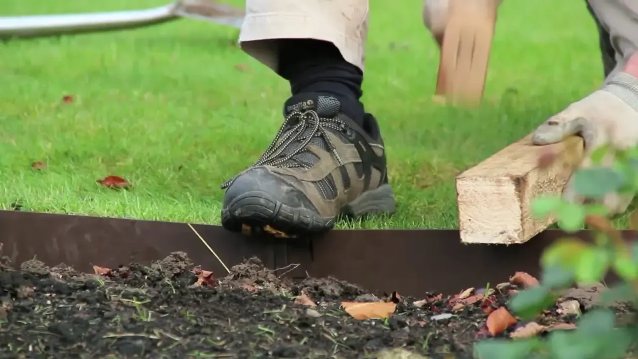 A person is laying a wooden plank on top of a lawn.