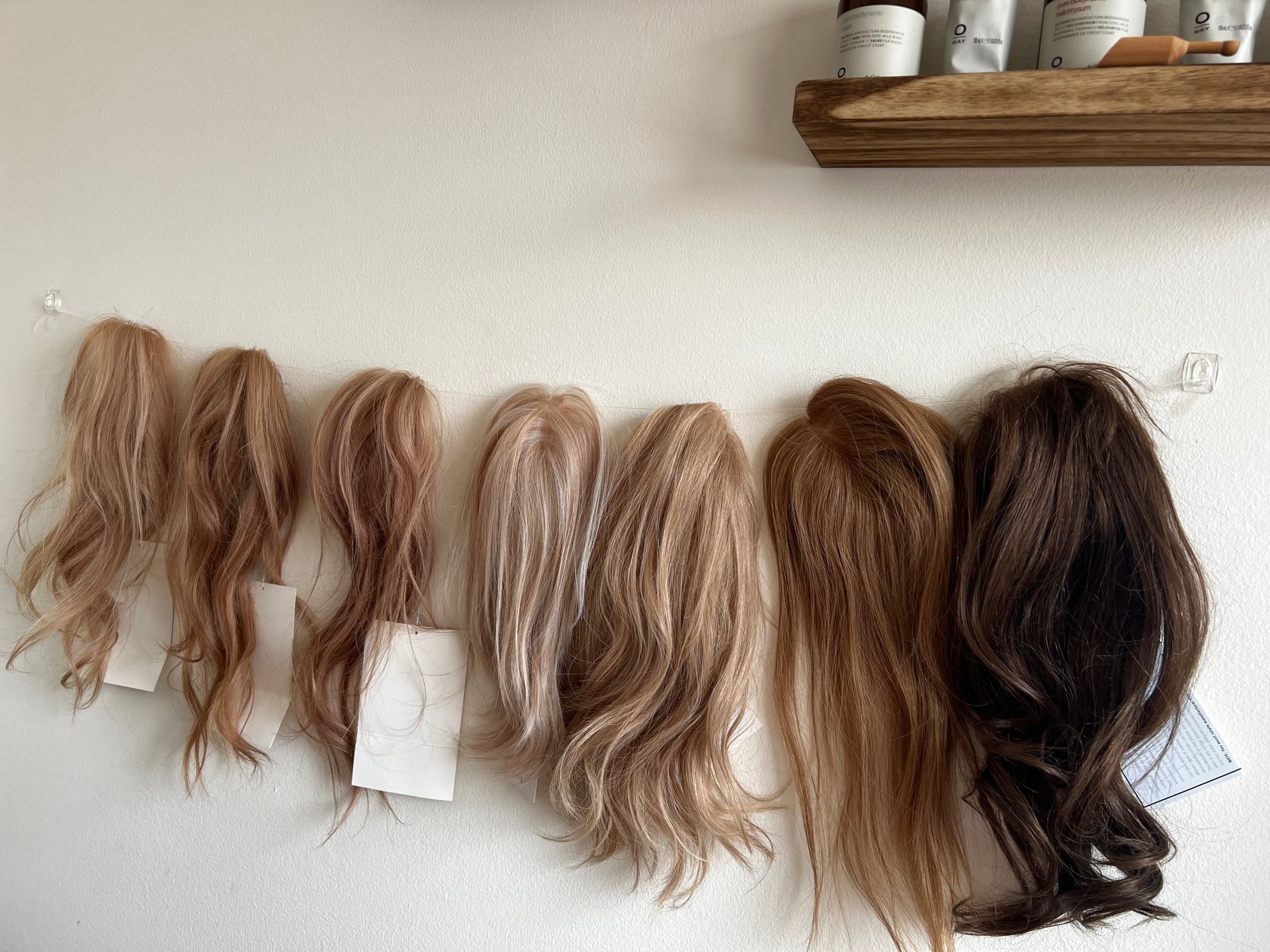A row of wigs hanging on a wall next to a shelf — St. Charles, IL — Studio Genesis - Hair Loss Solutions