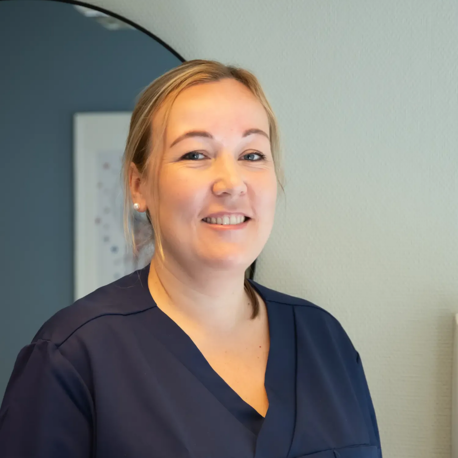 Tannlege Christian med briller og skjegg, iført blå skjorte og medisinsk maske, smiler til kameraet.