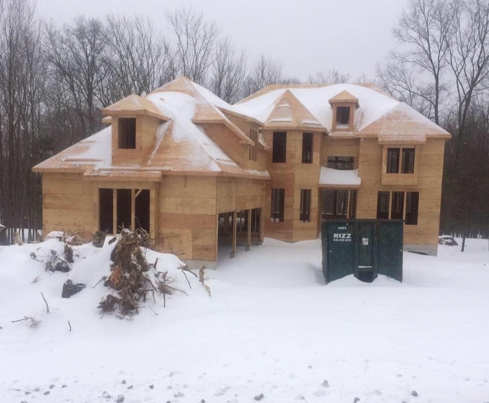 House under construction in a snowy landscape. Wooden frame with dormers and unfinished roof.