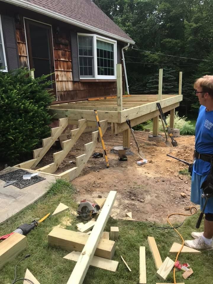 Deck construction in progress: Wooden structure with stairs, near a house with a person observing.