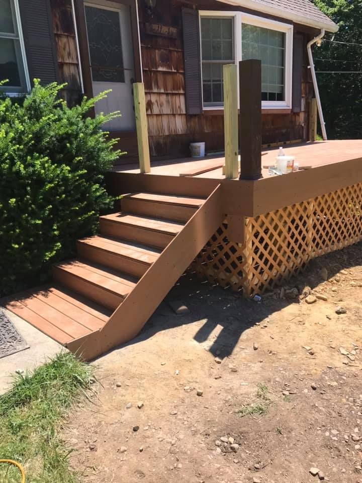 Brown wooden deck with steps and lattice railing, leading to a house entrance.