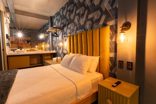 A hotel room with a bed , nightstand , and mirror.