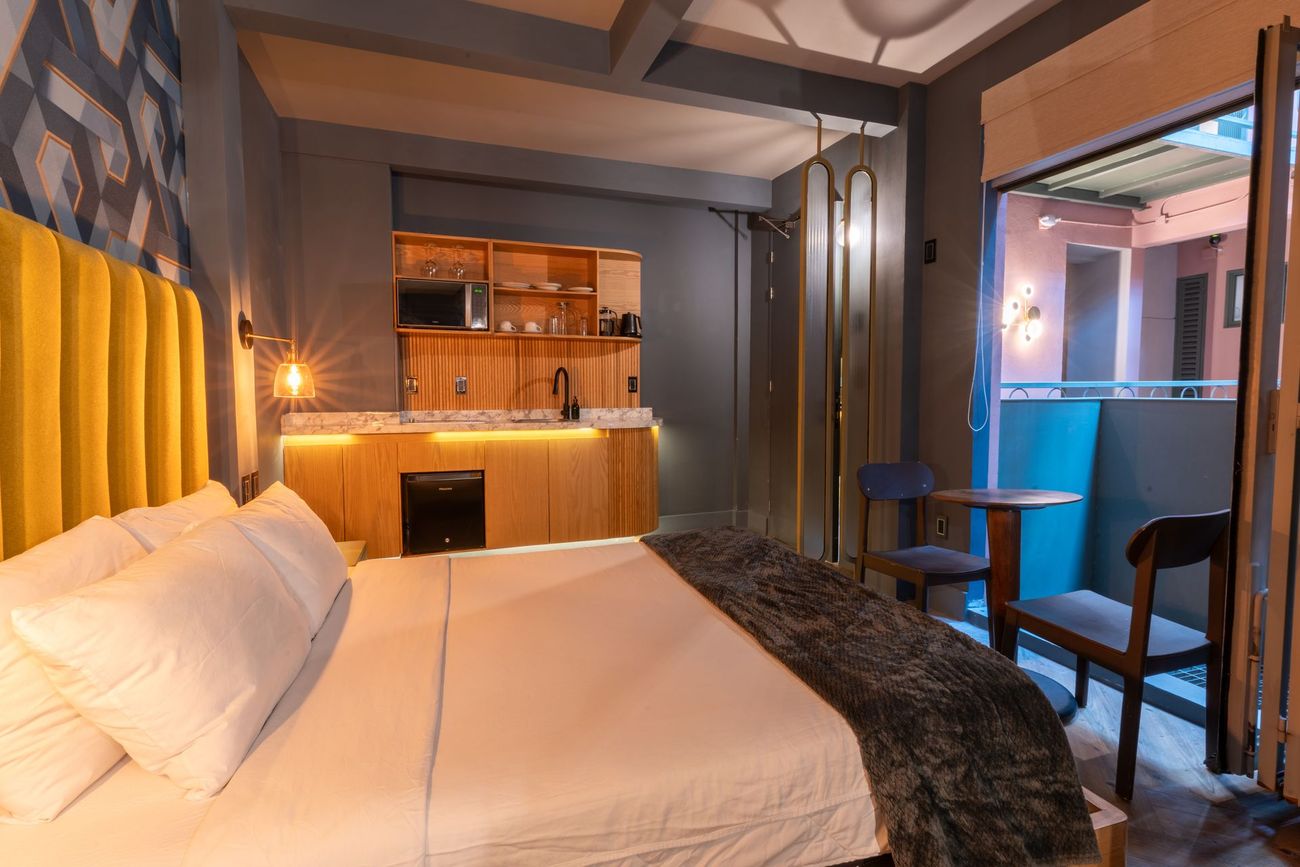 A hotel room with a bed , chairs , and a kitchen.