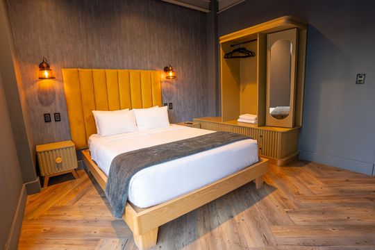 A hotel room with a bed , nightstand , wardrobe and mirror.