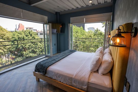 A bedroom with a large bed and a balcony with trees in the background.