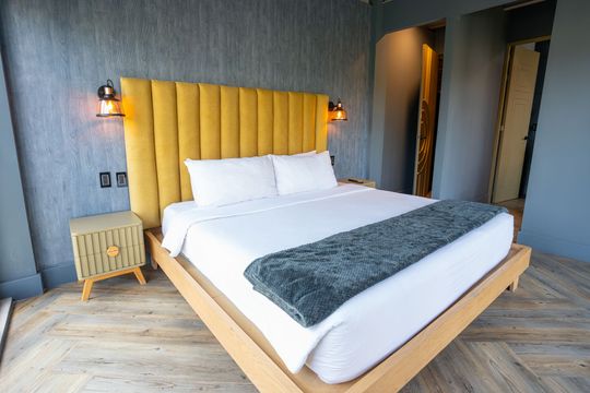 A hotel room with a king size bed and a yellow headboard.