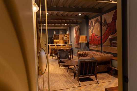 A living room with a couch , chairs , tables and paintings on the wall.