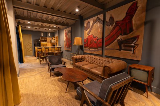 A living room with a couch , chairs , tables and paintings on the walls.