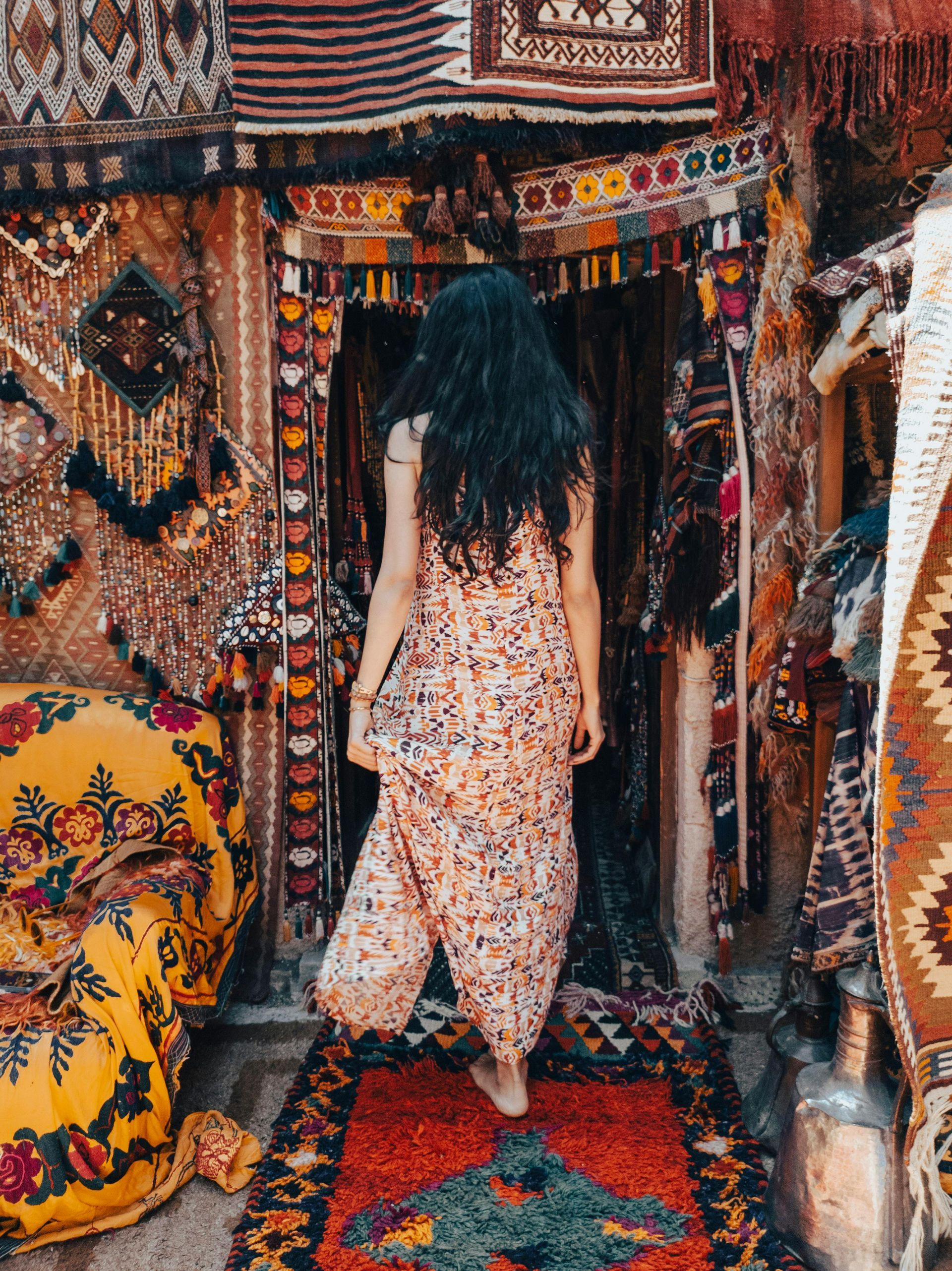 A woman in a dress is walking through a store filled with rugs.