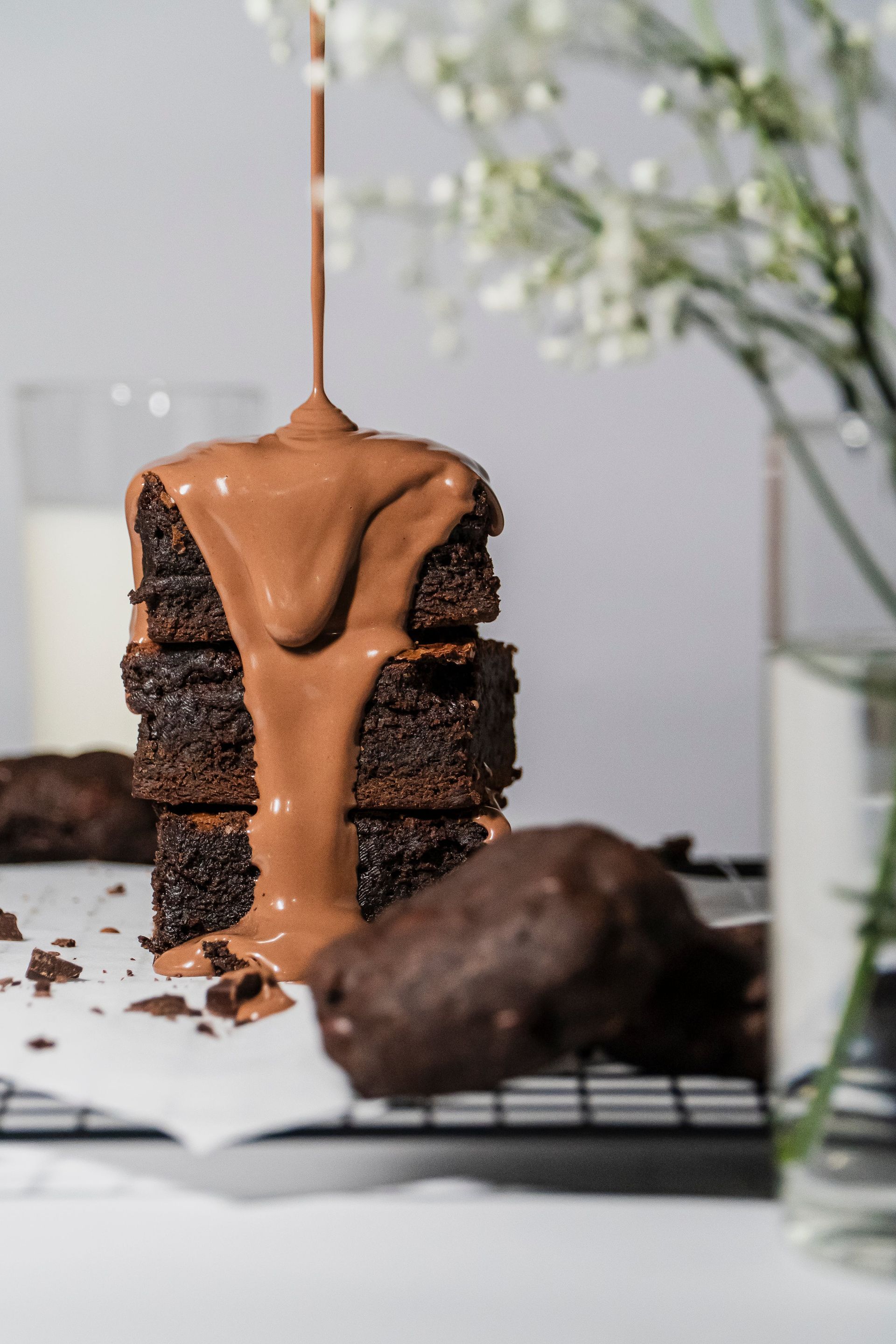 Chocolate sauce is being poured on a stack of brownies.