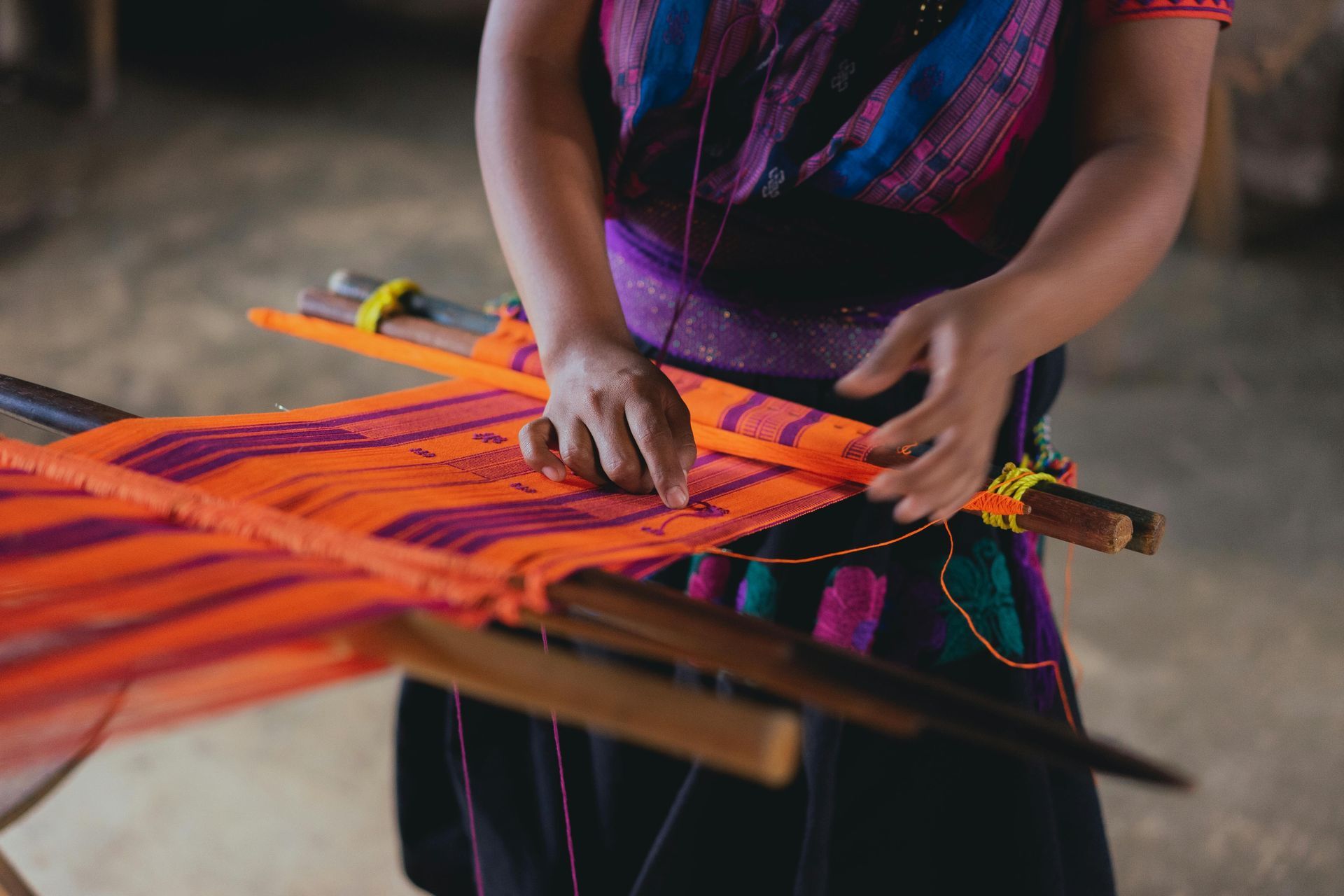 A woman in a purple dress is working on a loom.