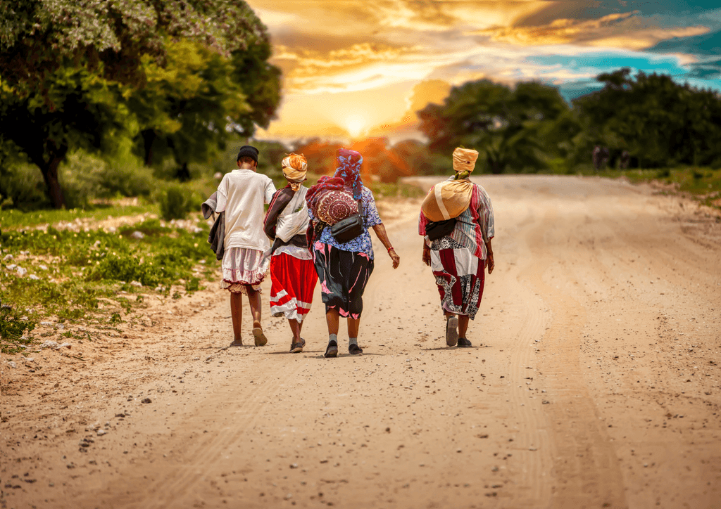 A group of people are walking down a dirt road at sunset.
