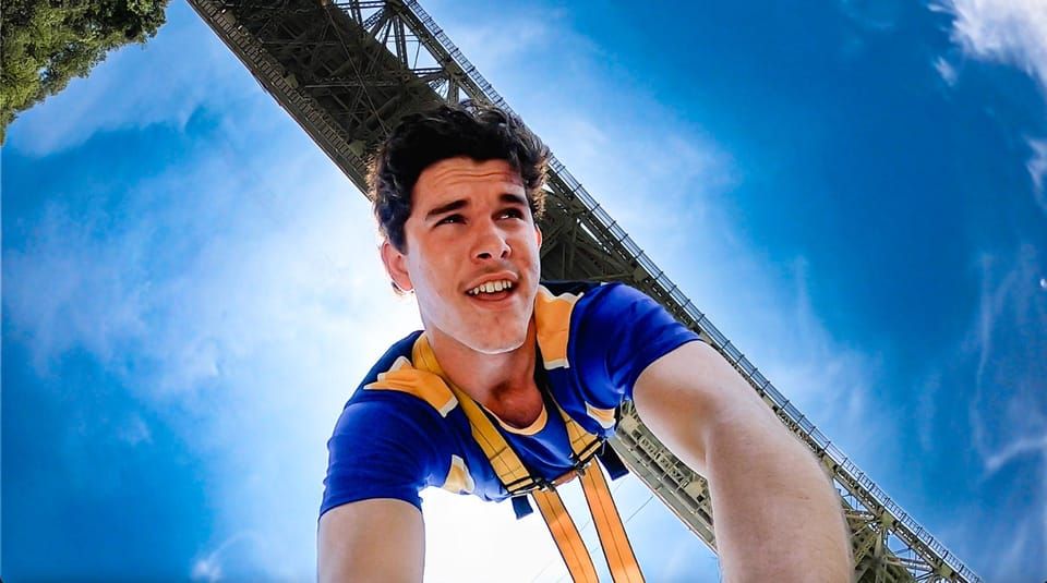 A man in a blue shirt and yellow harness is looking up at the sky.