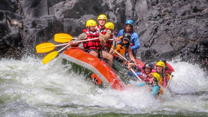 White water rafting. Raft of people navigating rapids, spray, and dark rock walls.