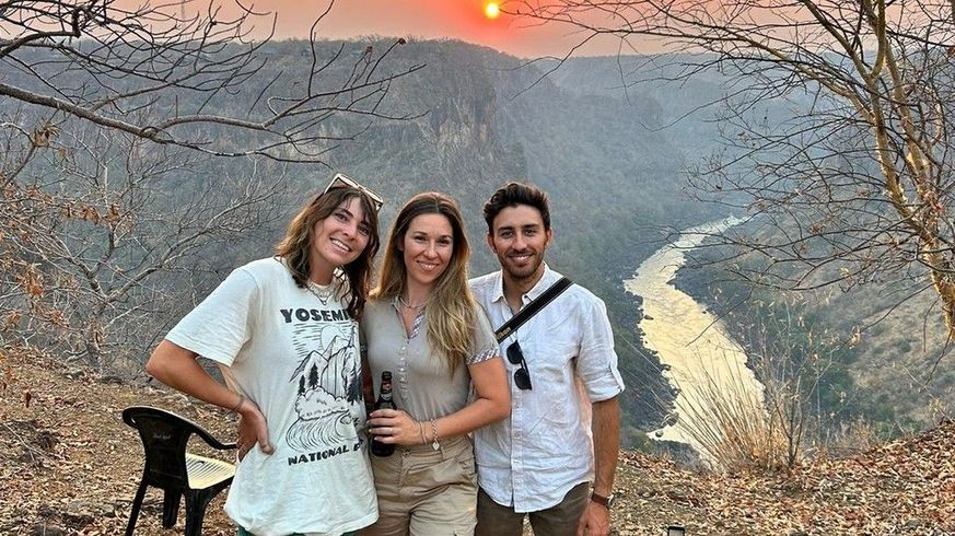 Three people pose for photo at sunset, overlooking a valley with river.