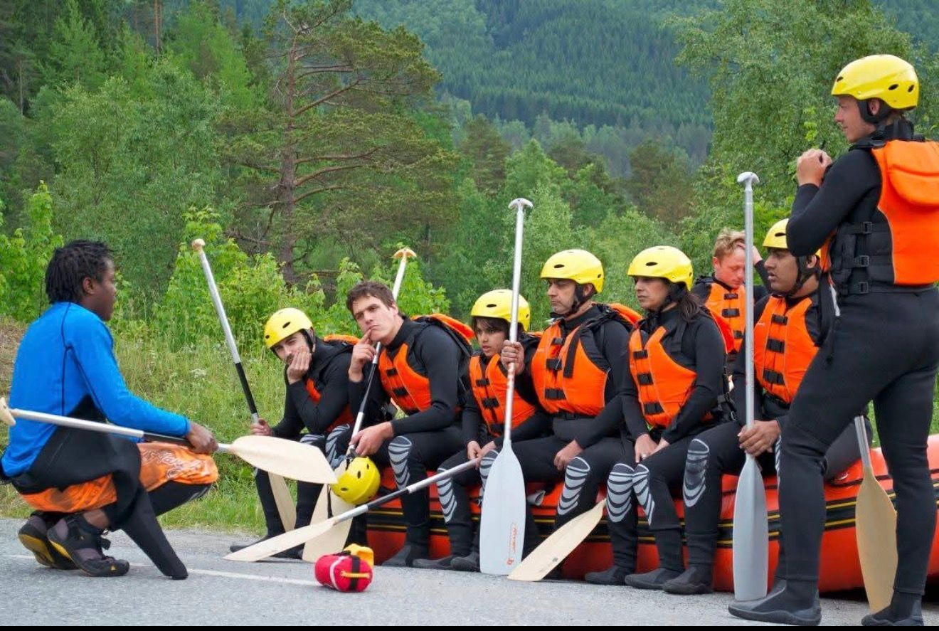 People in safety gear, including life vests and helmets, receive instructions before a rafting trip