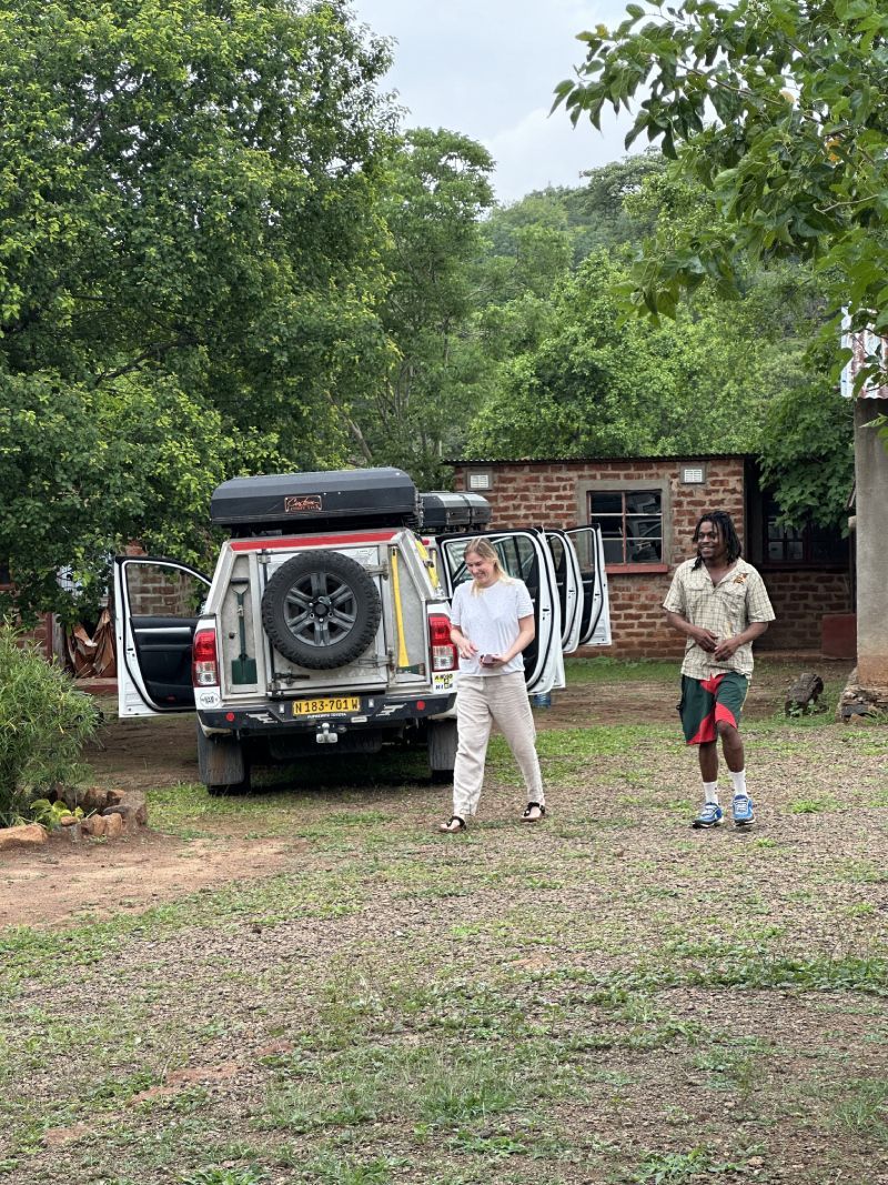 A white pickup truck with a roof tent parked outside, two people stand nearby.