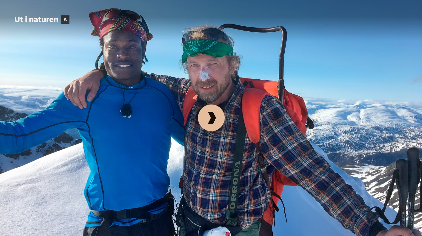 Two men on a snowy mountain top, one in blue, one in plaid. Both smiling, arms around each other.