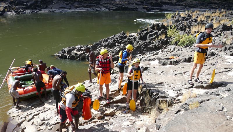 People preparing for whitewater rafting by a river.