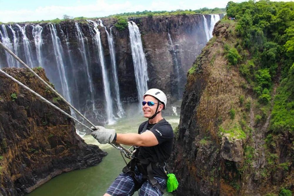 A man is hanging from a rope in front of a waterfall.