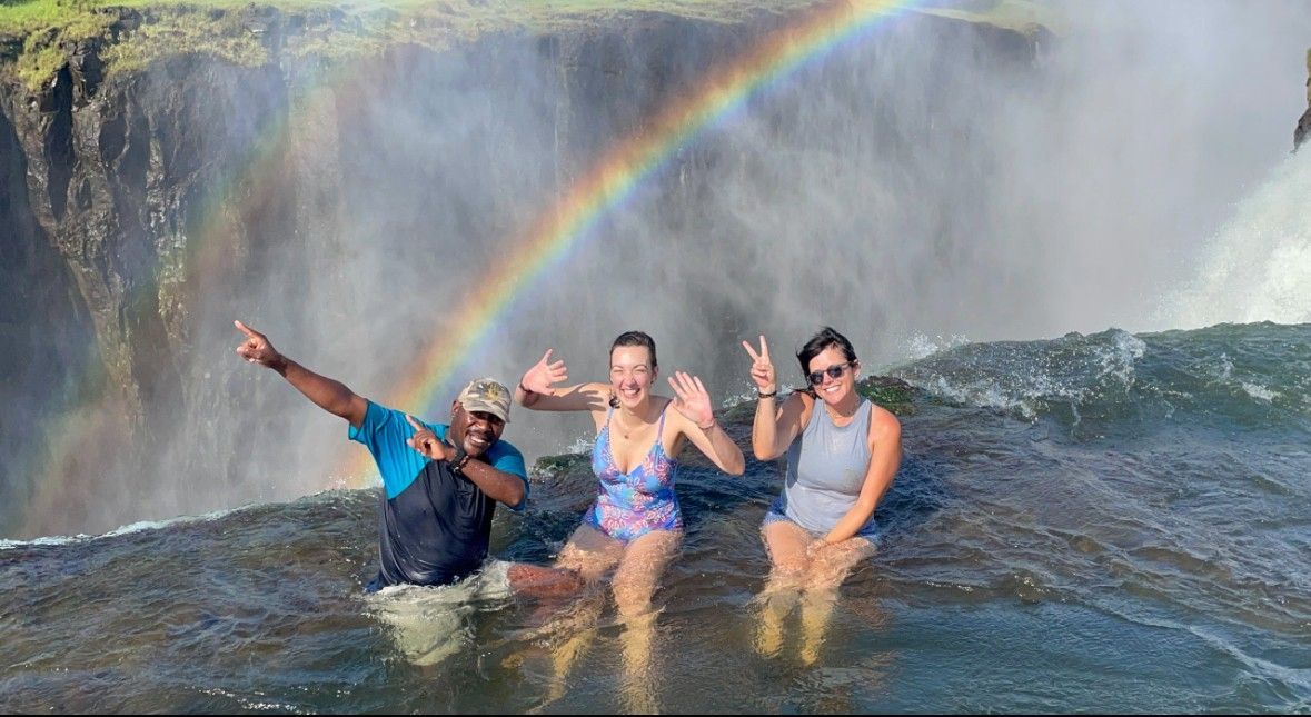 A group of people are standing in front of a waterfall with a rainbow in the background.