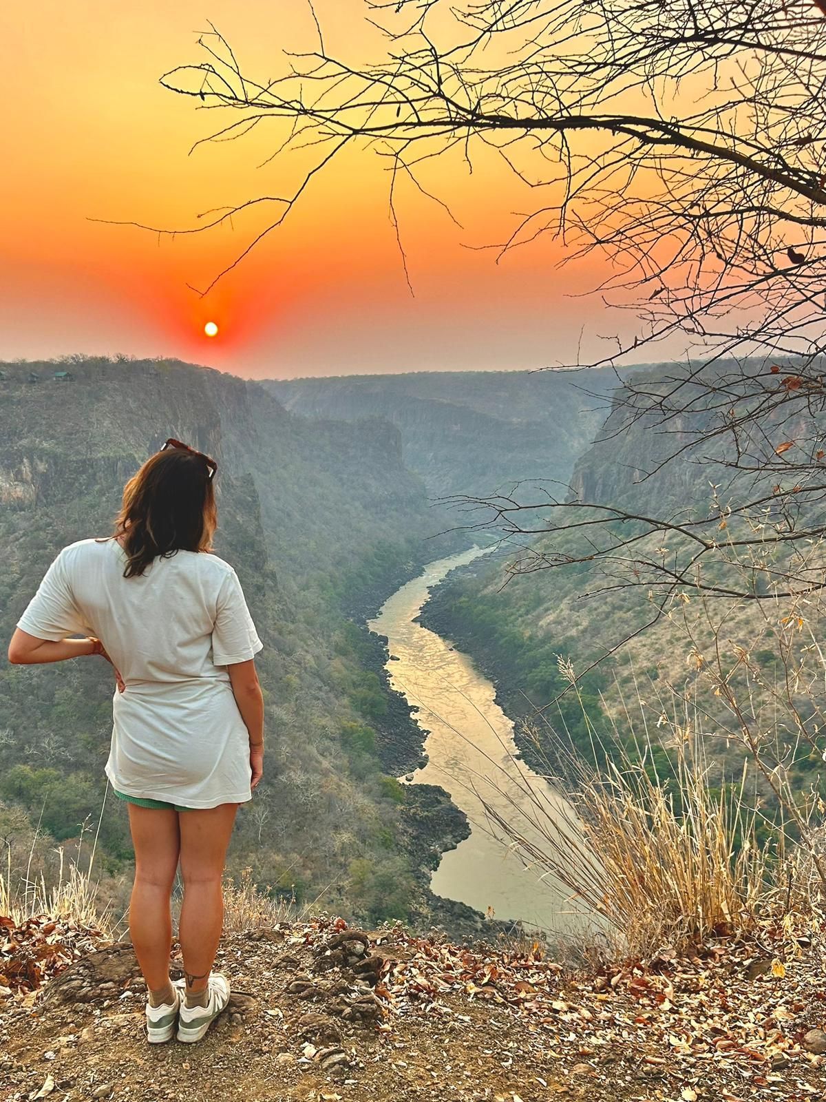 Three people on a raft in a river between cliffs, arms raised.