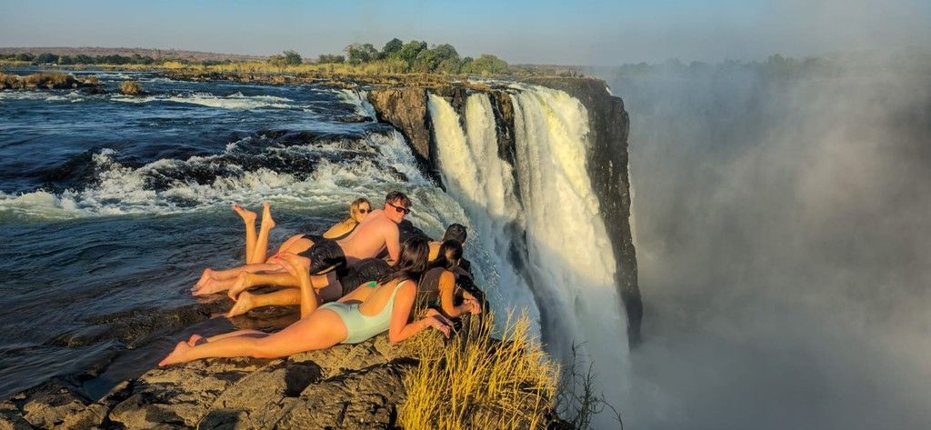 A group of people are laying on the edge of a waterfall.